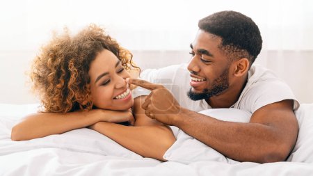 Téléchargez les photos : Affectueux couple afro-américain en interaction ludique tout en étant couché au lit, mettant en valeur l'amour et le bonheur - en image libre de droit