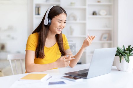 Joven asiática mujer casualmente vestida con auriculares en el uso de la computadora portátil para una videollamada, estudiante tiene lección en línea