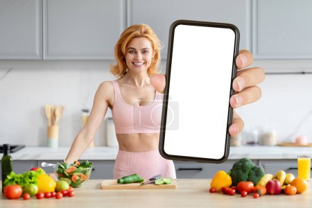 Fit woman in sporty outfit showcasing a blank smartphone screen with healthy food backdrop
