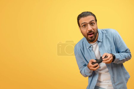 Foto de Un joven indio que expresa sorpresa y diversión mientras sostiene un controlador de juego sobre un fondo amarillo - Imagen libre de derechos