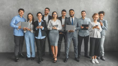 Photo for A group of young professionals in smart casual attire stand together, holding laptops and smiling, representing a tech-savvy workforce - Royalty Free Image