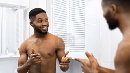 A bare-chested African american man gives a thumbs-up to his reflection, symbolizing self-satisfaction and a positive self-image