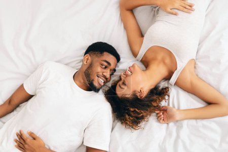 Blick von oben auf ein afrikanisch-amerikanisches Paar, das sich auf dem Bett zärtlich umarmt, was Zuneigung und Komfort in Beziehungen hervorhebt
