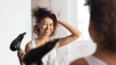 Photo for Smiling afro girl drying her hair in front of mirror in bathroom. - Royalty Free Image