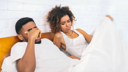 Photo for Relationships difficulties, stress and impotence. Black couple having marital problems. Woman in bed looking under blanket, man with erectile dysfunction - Royalty Free Image