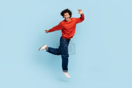 Foto de Joven afroamericano alegre con el pelo rizado saltando en el aire expresando euforia - Imagen libre de derechos