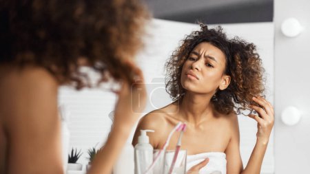 Afro-american girl frowning and looking intently on her face in mirror. Skin problem concept