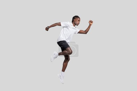 Young African American guy with athletic build captured in mid-air, exemplifying dynamics and energy against a plain background