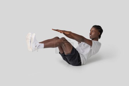 Athletischer afroamerikanischer Mann in einer herausfordernden V-Sit-Core-Trainingspose mit ausgestreckten Beinen und konzentriertem Ausdruck