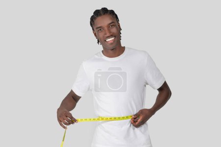 Lächelnder Afroamerikaner misst stolz seine Taille und präsentiert Fitness und Gesundheit auf weißem Hintergrund