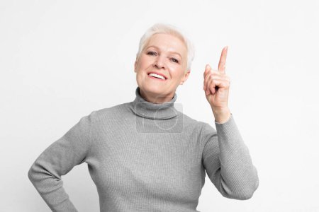 Eine fröhliche Seniorin, ältere Europäerin mit erhobenem Zeigefinger, schlägt vor, eine Idee oder einen Punkt zu haben, die s3niorlife-Weisheit reflektiert