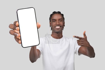 Cheerful African American man pointing at a smartphone with blank white screen for mockup on white background