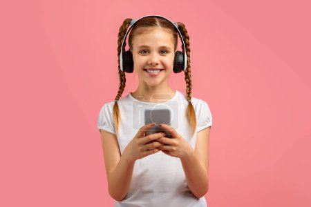 Mädchen mit geflochtenen Haaren hält Smartphone und trägt Kopfhörer auf rosa Hintergrund, sieht zufrieden aus