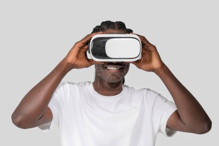 Foto de Joven afroamericano inmerso en una experiencia virtual, sosteniendo un auricular VR con un fondo liso, subrayando la moderna tecnología de entretenimiento - Imagen libre de derechos