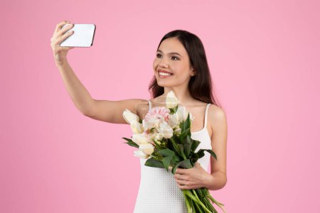 A smiling lady takes a selfie with a large bouquet, the epitome of european summer. An isolated Generation Z woman against a pink background