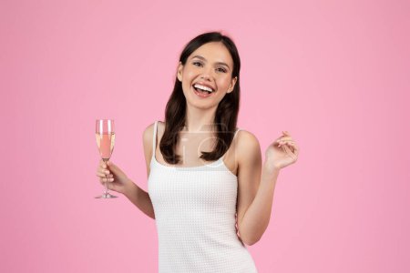 Téléchargez les photos : Une dame exubérante tenant une flûte de champagne, incarnant l'esprit de célébration et d'été, idéale pour l'imagerie de la génération Z, isolée sur rose - en image libre de droit