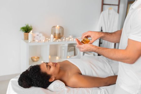 The hands of a therapist carefully pour golden essential oil for a massage therapy session in a well-appointed spa