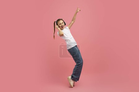 Téléchargez les photos : Une jeune fille exubérante saute dans l'air avec joie, donnant un sentiment de liberté sur un fond de studio rose - en image libre de droit