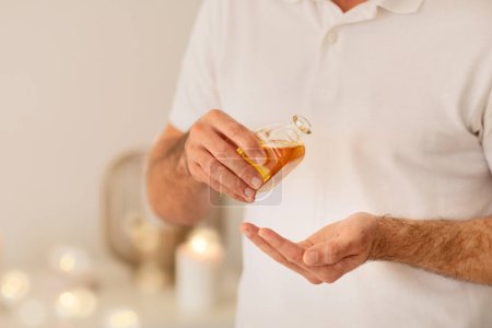Téléchargez les photos : Les mains d'un masseur homme sont présentées tenant une bouteille d'huile dorée, mettant l'accent sur un thème de spa et de soins de la peau - en image libre de droit