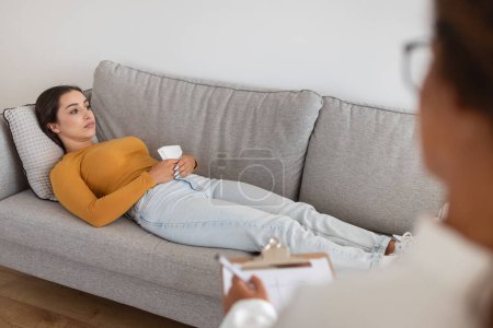 Foto de Una mujer se acuesta en un sofá mientras discute temas con un terapeuta en un entorno tranquilo. Depresión, ansiedad - Imagen libre de derechos