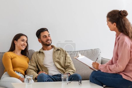 Ein Paar sitzt auf einem Sofa und wirkt aufmerksam und zufrieden, wenn es einem Therapeuten während einer Familiensitzung zuhört.