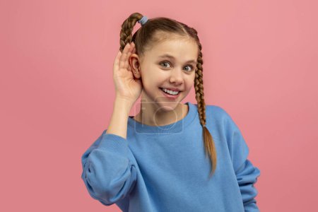 Attentive girl with hand to ear simulates listening or hearing something, on a vivid pink background