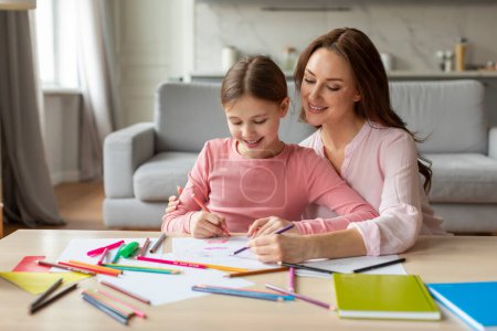Téléchargez les photos : Mère aide sa fille avec les devoirs, partageant un moment d'apprentissage proche et joyeux à l'intérieur confortable de la maison, l'espace de copie - en image libre de droit