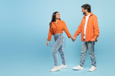 Photo for Indian man and woman in casual wear holding hands and exchanging a tender look full of connection on blue - Royalty Free Image