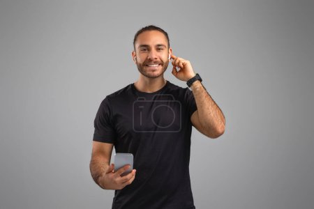 Hombre alegre haciendo una llamada telefónica en su teléfono inteligente, representado en un momento casual y conectado en un fondo gris