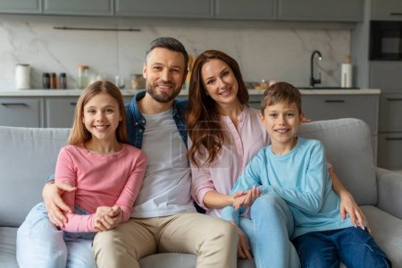 A cheerful family of four with two children sitting on a couch, smiling at the camera in a home setting