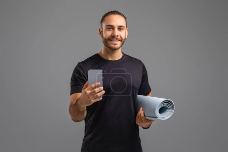 Photo for A content man in sportswear holds a yoga mat and smartphone, possibly managing his workout routine - Royalty Free Image