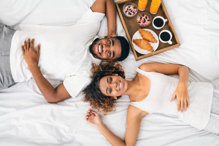 Téléchargez les photos : Heureux couple afro-américain couché dans la chambre avec plateau de petit déjeuner, vue sur le dessus - en image libre de droit