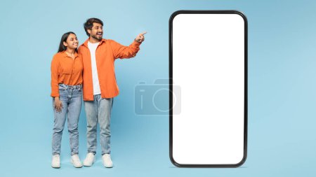 Téléchargez les photos : Écran de smartphone vierge avec couple indien en arrière-plan pointant avec enthousiasme vers le côté, idéal pour les annonces - en image libre de droit