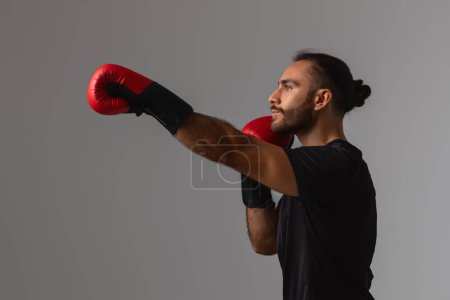 Foto de Un atleta enfocado está practicando sus habilidades de perforación usando vibrantes guantes de boxeo rojos en un espacio neutral - Imagen libre de derechos