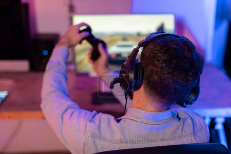 Gamer-Mann mit Kopfhörer reckt die Arme in die Luft, hinter einem Computermonitor, Rückseite