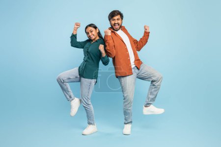 Foto de Enérgica y feliz pareja india celebrando, posando con los puños levantados en una postura de victoria sobre el azul - Imagen libre de derechos