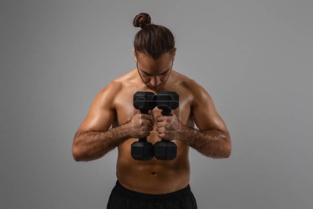 An athletic guy indulges in bicep curls using black dumbbells, highlighting his muscular back and arms