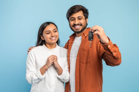 Content Indian couple showing off a car key, implying a new vehicle purchase or ownership on blue
