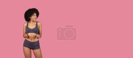 Foto de Juguetona joven mujer negra en traje deportivo haciendo gestos hacia sí misma sobre un fondo rosa - Imagen libre de derechos