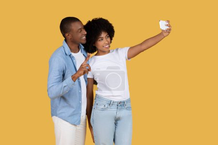 Pareja joven afroamericana con trajes elegantes posando para una selfie, capturando un momento alegre juntos