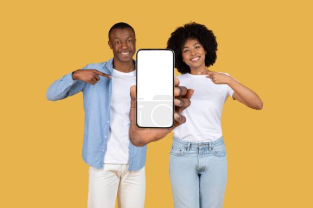 Téléchargez les photos : Afro-Américain homme et femme en tenue décontractée tenant un smartphone montrant écran vide vers la caméra - en image libre de droit