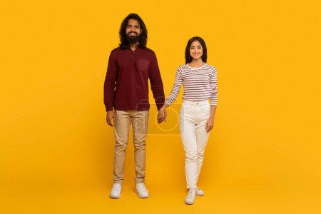 Téléchargez les photos : Un homme et une femme tenant la main et debout côte à côte contre un mur jaune uni, représentant la compagnie - en image libre de droit