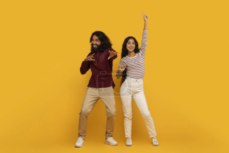 Photo for Happy and energetic couple with trendy clothes dancing joyfully against a bold yellow background - Royalty Free Image