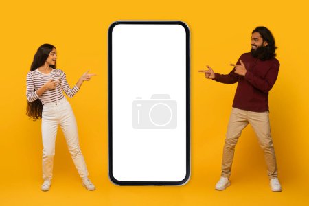 Lächelnd interagieren Mann und Frau und zeigen auf einen leeren, übergroßen Smartphone-Bildschirm auf gelbem Hintergrund.