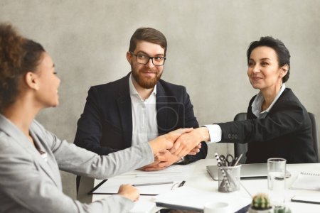 Foto de Tres profesionales en una sala de reuniones, una mujer y dos hombres, estrechando las manos de acuerdo - Imagen libre de derechos