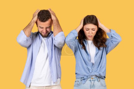 Foto de Dos adultos expresan frustración con las manos en la cabeza sobre un fondo amarillo - Imagen libre de derechos