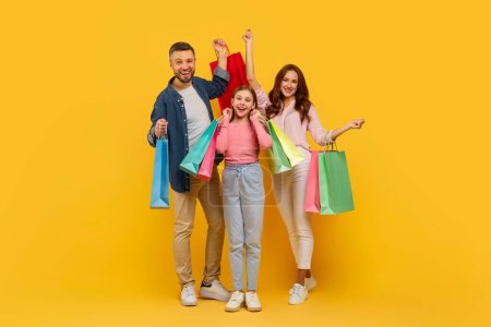 An overjoyed family with their arms triumphantly raised, holding shopping bags on a yellow background, symbolizing happiness
