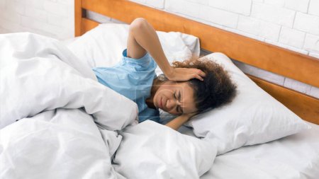 Téléchargez les photos : Femme couvrant ses oreilles, se réveillant du bruit, couchée au lit le matin - en image libre de droit