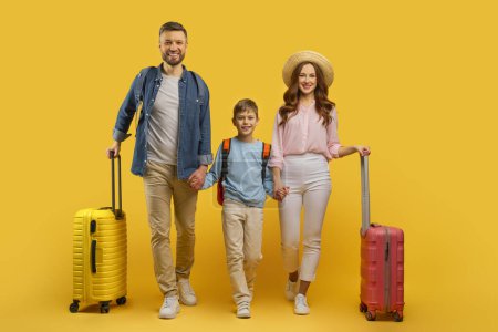 Foto de Familia sonriente de tres, padres e hijo, que sostiene maletas contra un fondo amarillo, listo para viajar de vacaciones - Imagen libre de derechos