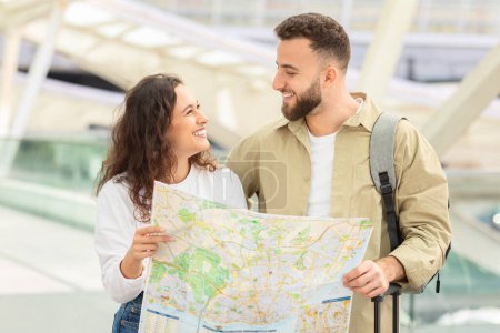 Téléchargez les photos : Couple aimant partager un moment joyeux comme ils se regardent sur une carte, suggérant des plans de voyage partagés dans les environs de l'aéroport - en image libre de droit